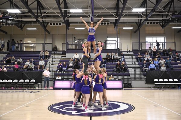 Cheer team performs tower stunt during stoppage of basketball game.